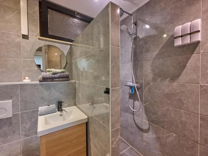 Bathroom with grey tiles, a washbasin unit with a wooden front and a walk-in rain shower.