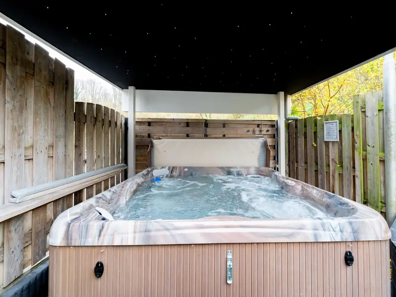 Jacuzzi met bruisend water onder een donker dak met kleine lichtjes, tussen houten schuttingen.