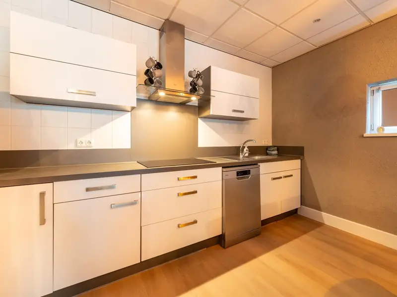 White kitchen with hob, steel extractor hood flanked by mug trees, sink and dishwasher.