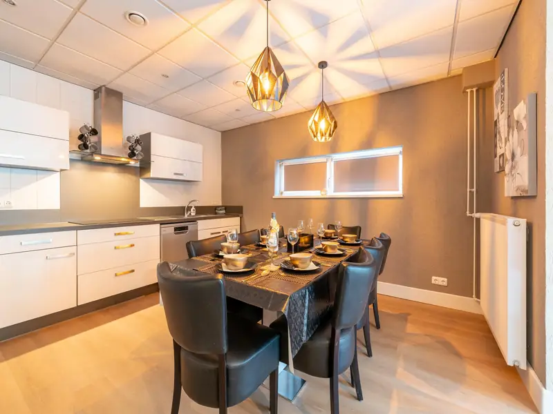 Witte keuken met afzuigkap en een gedekte eettafel met zwarte leren stoelen.