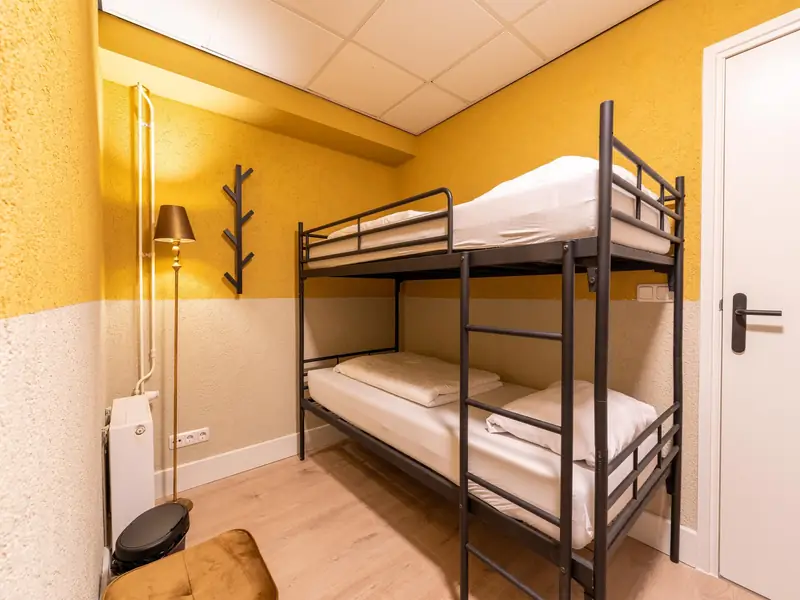 Kleine slaapkamer met zwart metalen stapelbed, staande lamp en gele muren.