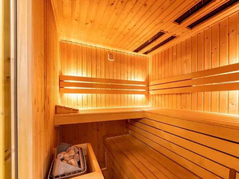 Wooden sauna with tiered benches, a stove with stones and lighting behind the backrests.