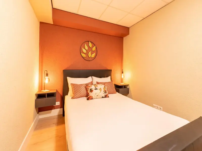 Bedroom with a double bed, terracotta wall, golden leaf decoration and two bedside lamps.