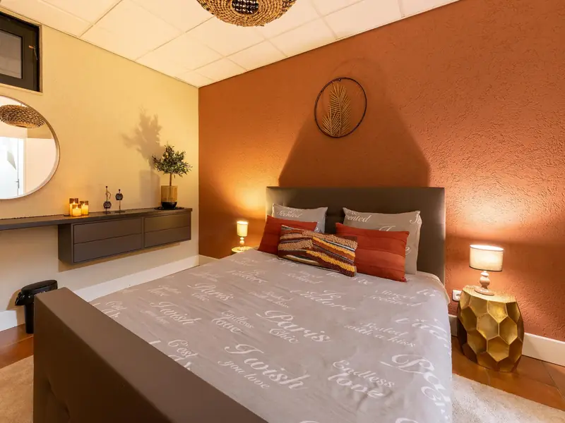 Bedroom with a double bed, terracotta wall, round mirror and gold side table.