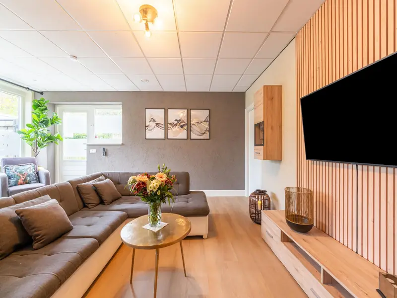 Grey corner sofa, round gold coffee table and a TV on a slatted wooden wall.