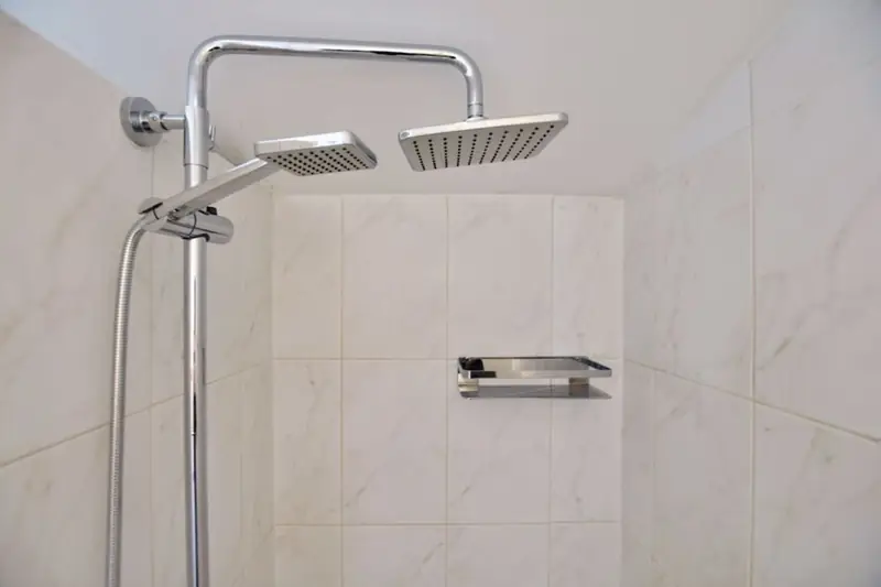 Verchromte Duschsäule mit eckiger Regenbrause, Handbrause und einer Wandablage.