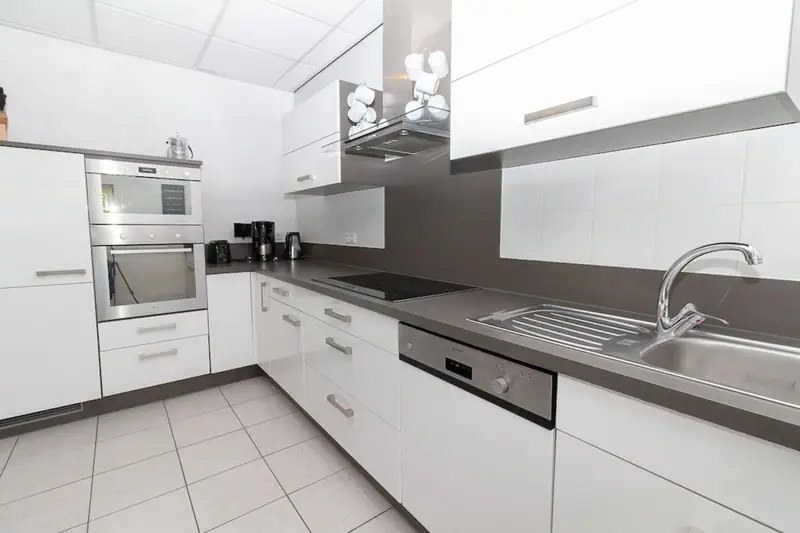 Keuken met witte kasten, kookplaat, spoelbak, vaatwasser, inbouwoven en koffiezetapparaat.