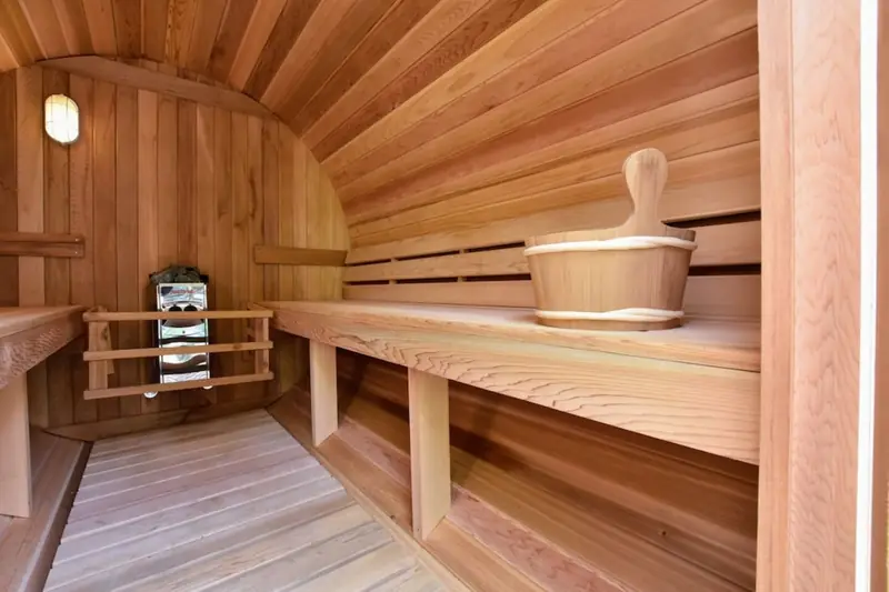 Im Inneren der Fasssauna: Holzbänke an der runden Wand, ein Saunaofen und ein Holzkübel.