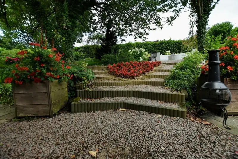 Grindtreden met lage randen lopen omhoog langs een perk rode bloemen en houten plantenbakken.