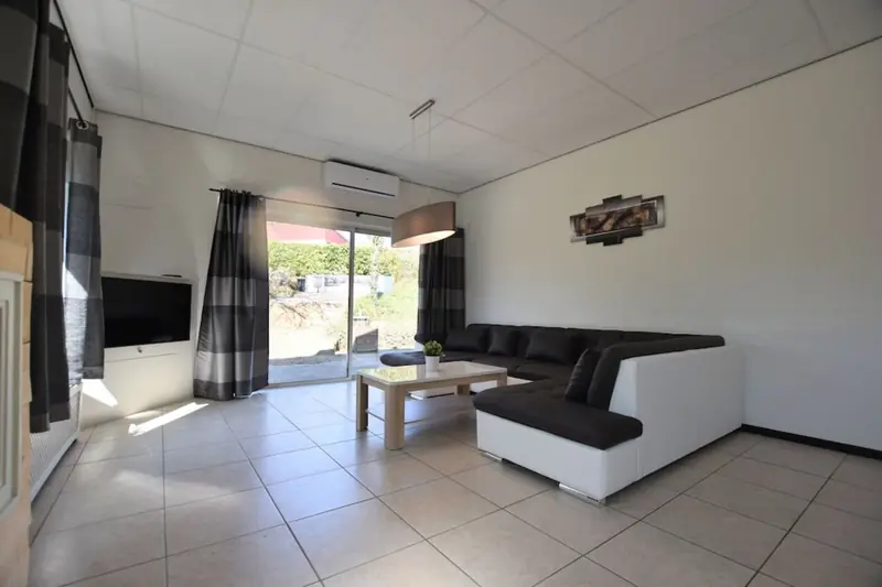 Wohnzimmer mit großem Ecksofa, Couchtisch, Fernseher und Schiebetür nach draußen.
