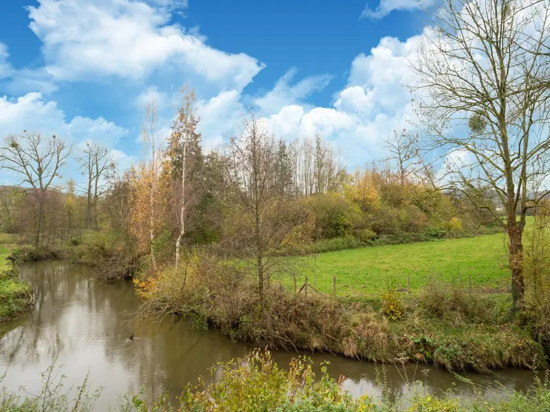 A winding river beside a green meadow with a wire fence and trees.